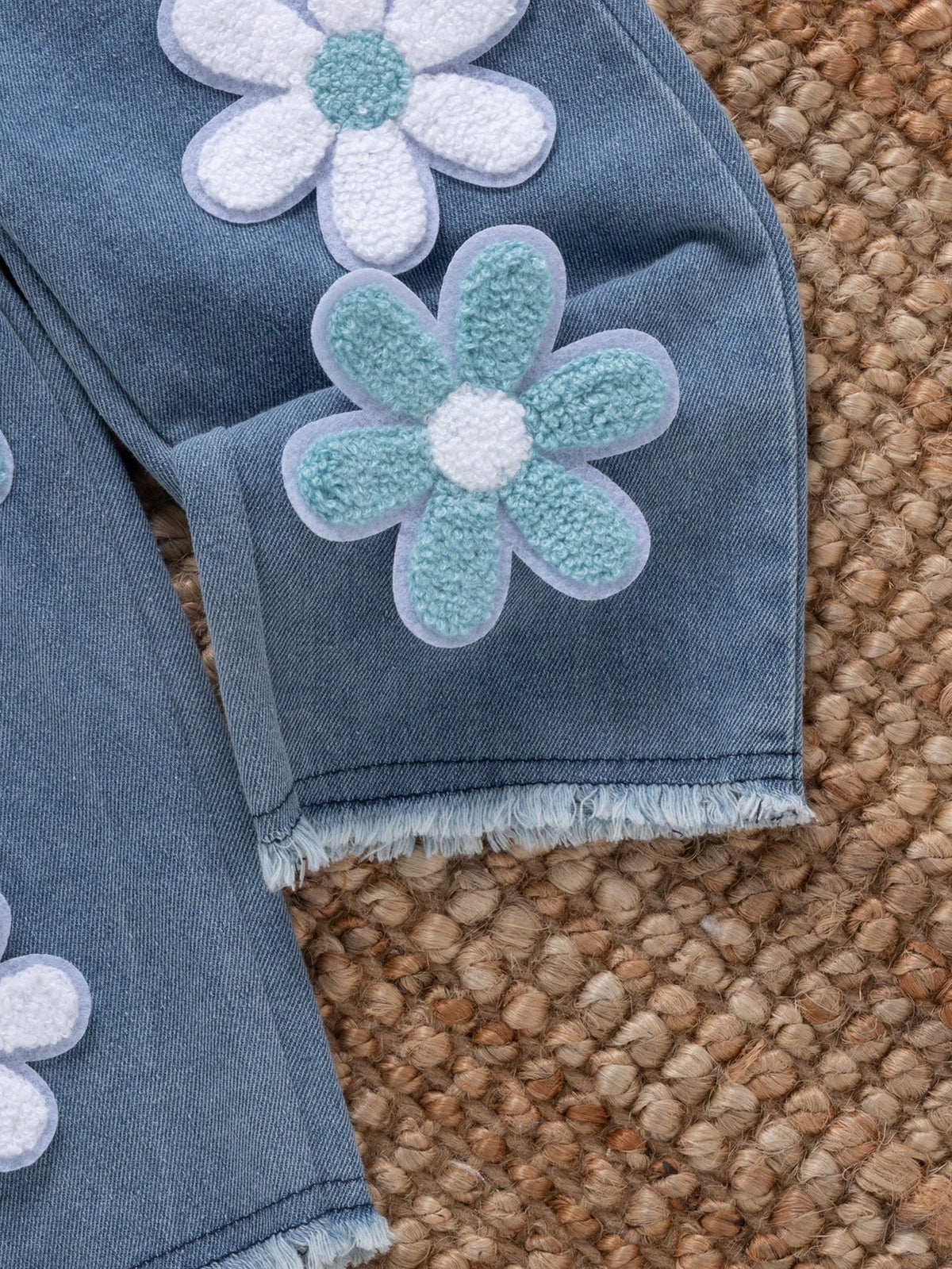 Pantalón de mezclilla azul para bebé con flores blancas y celestes en relieve y ruedos deshilachados.