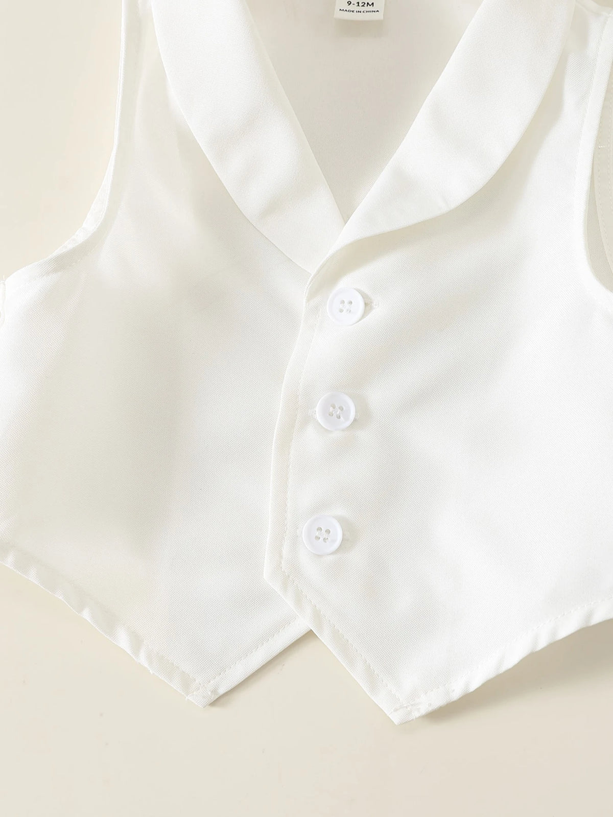 Chaleco blanco para bebe con cuello de solapa, tres botones frontales y terminación en punta.
