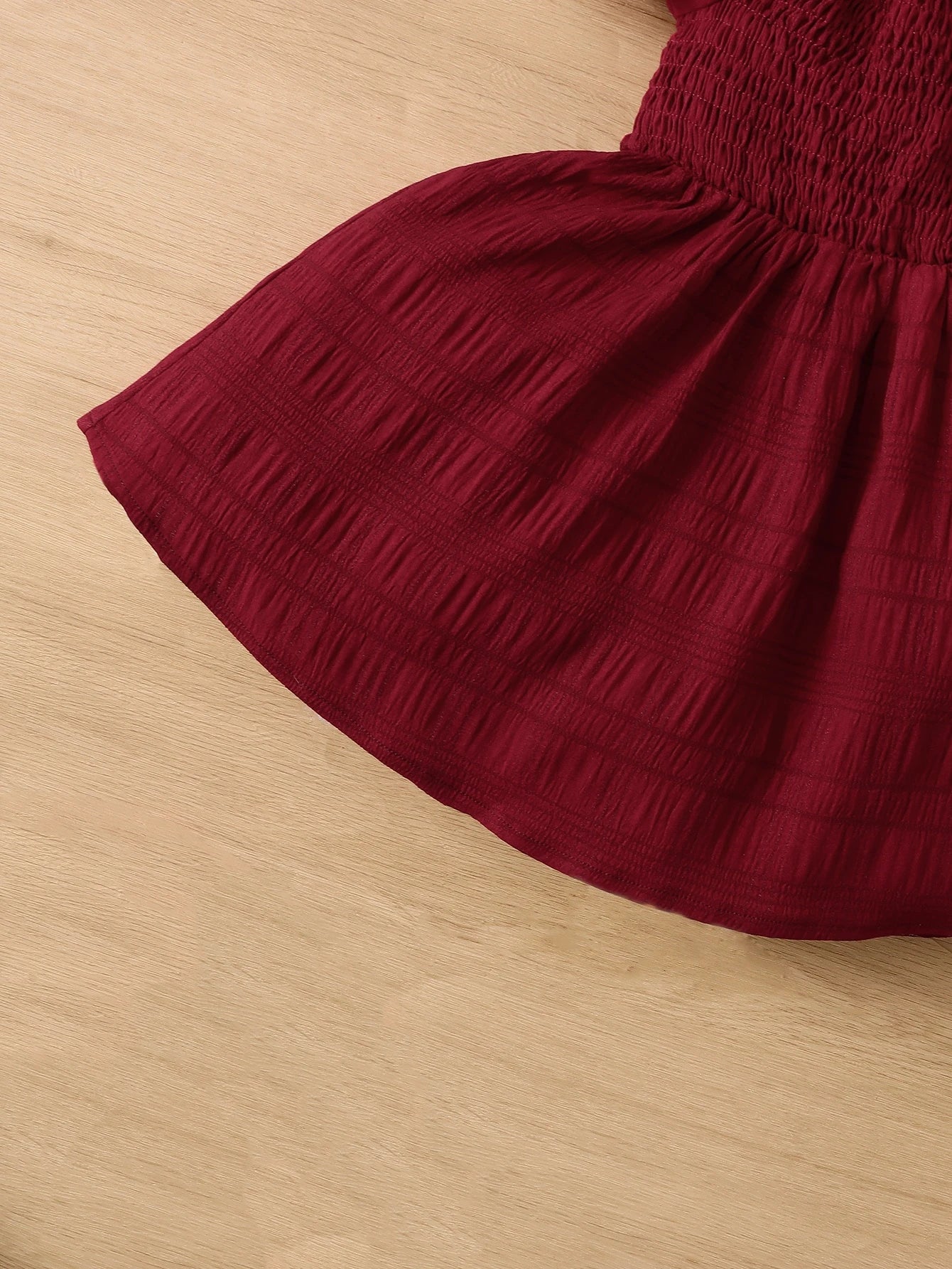 Prenda burdeos vestido para bebe vista completa frontal sobre fondo de madera