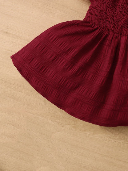 Prenda burdeos vestido para bebe vista completa frontal sobre fondo de madera