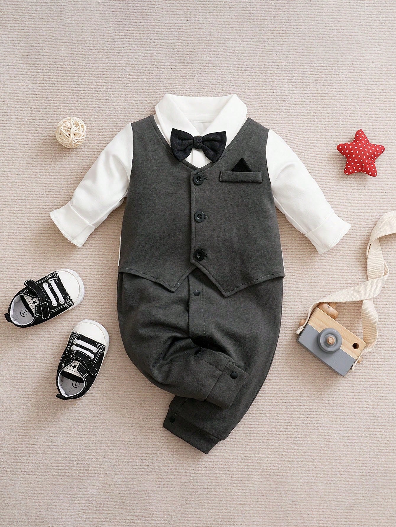 Prenda gris mameluco para bebe con detalle de cuello blanco, chaleco y moño negro