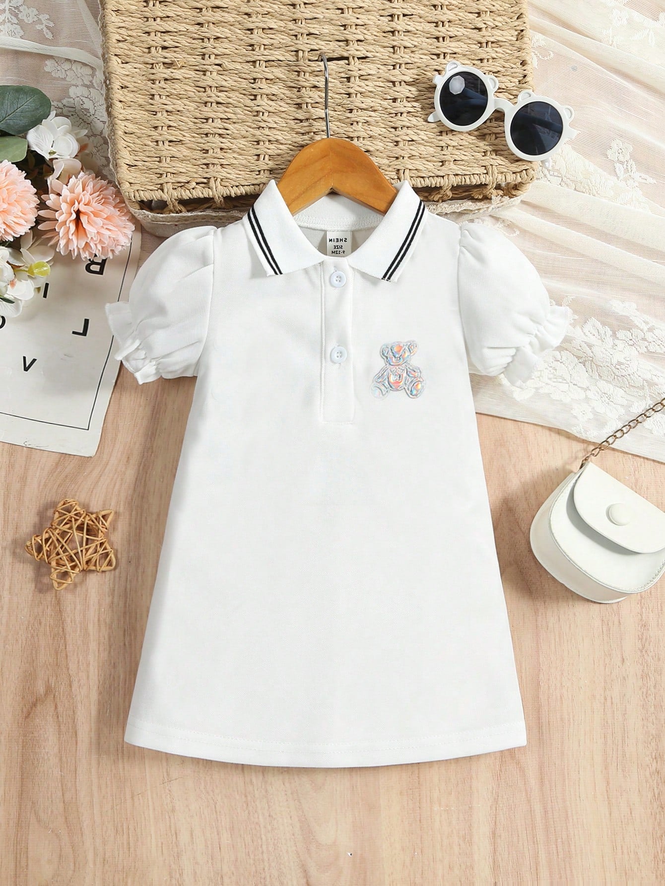 Prenda blanca vestido polo para bebe, vista frontal con parche de oso tornasol