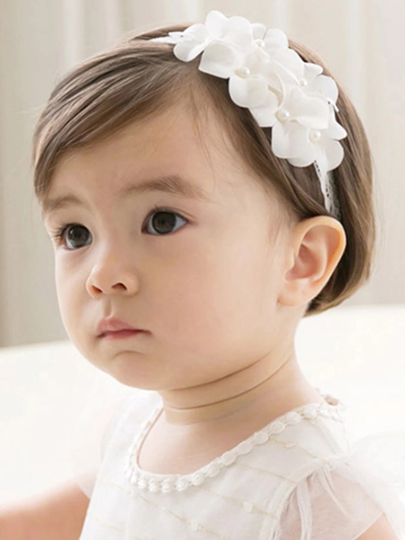 Prenda blanca diadema para bebe con flores decorativas vista frontal
