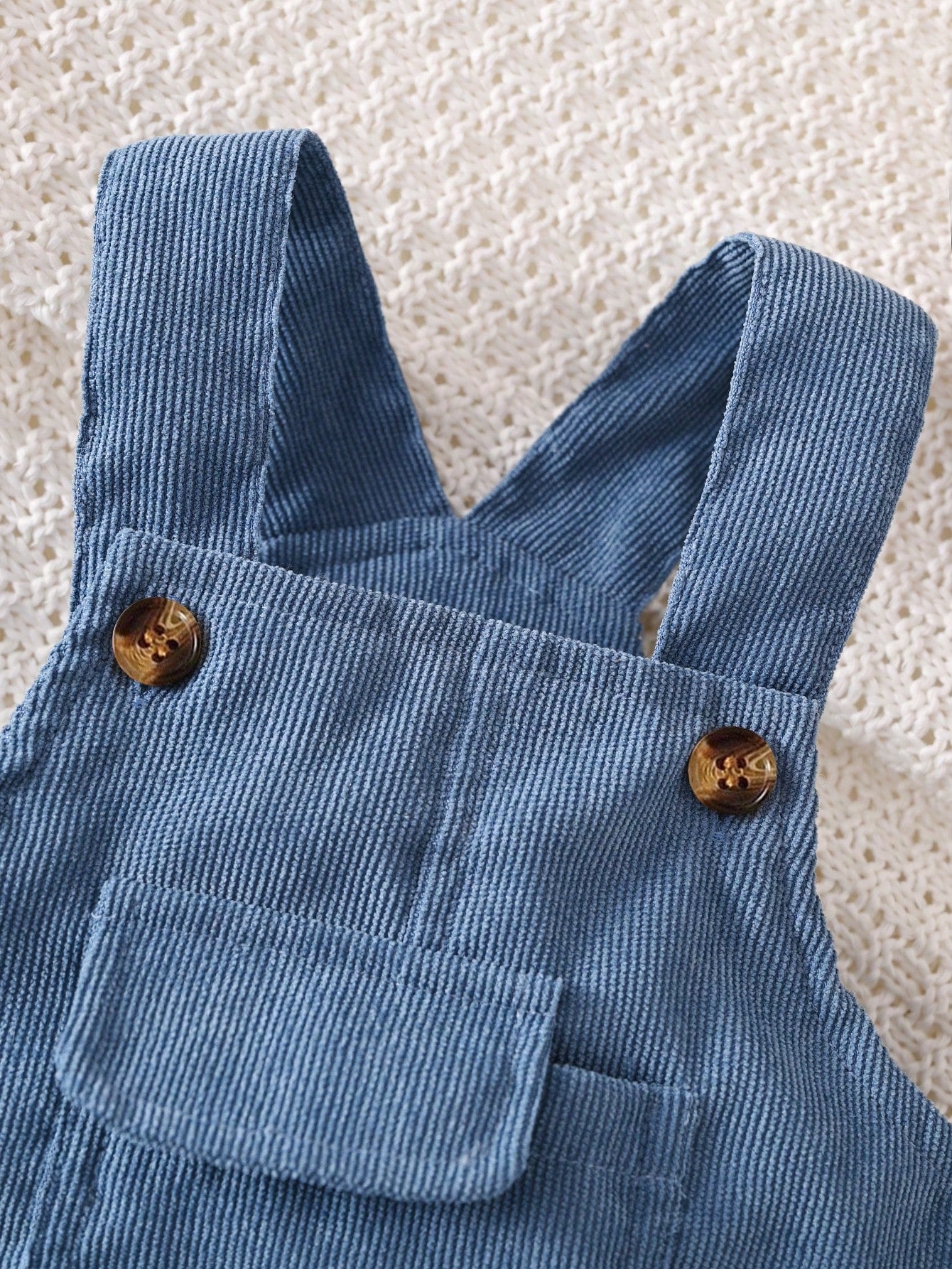 Prenda azul overol para bebe detalle del bolsillo frontal con solapa