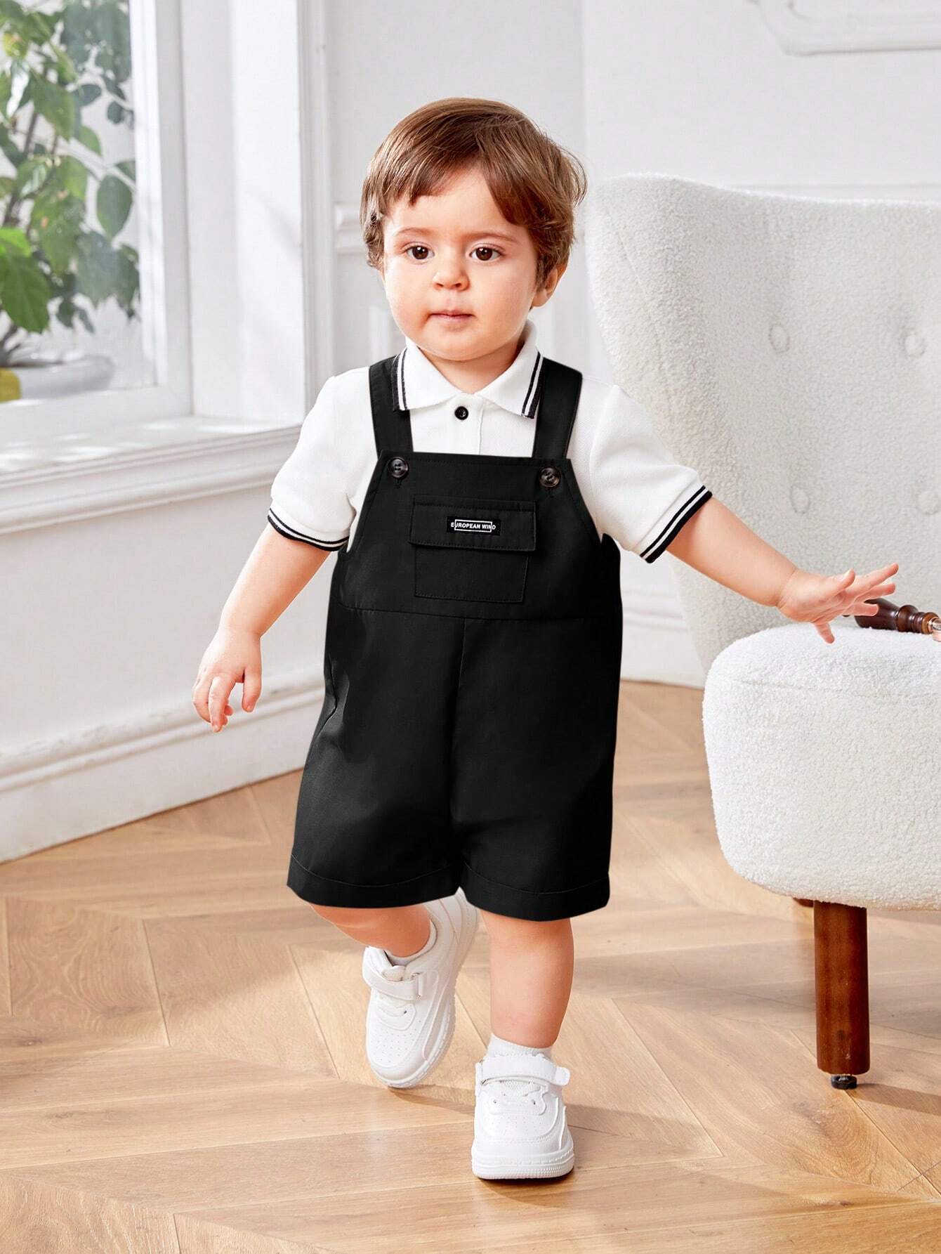 Prenda blanca y negra conjunto polo con overol para bebe colgado vista frontal