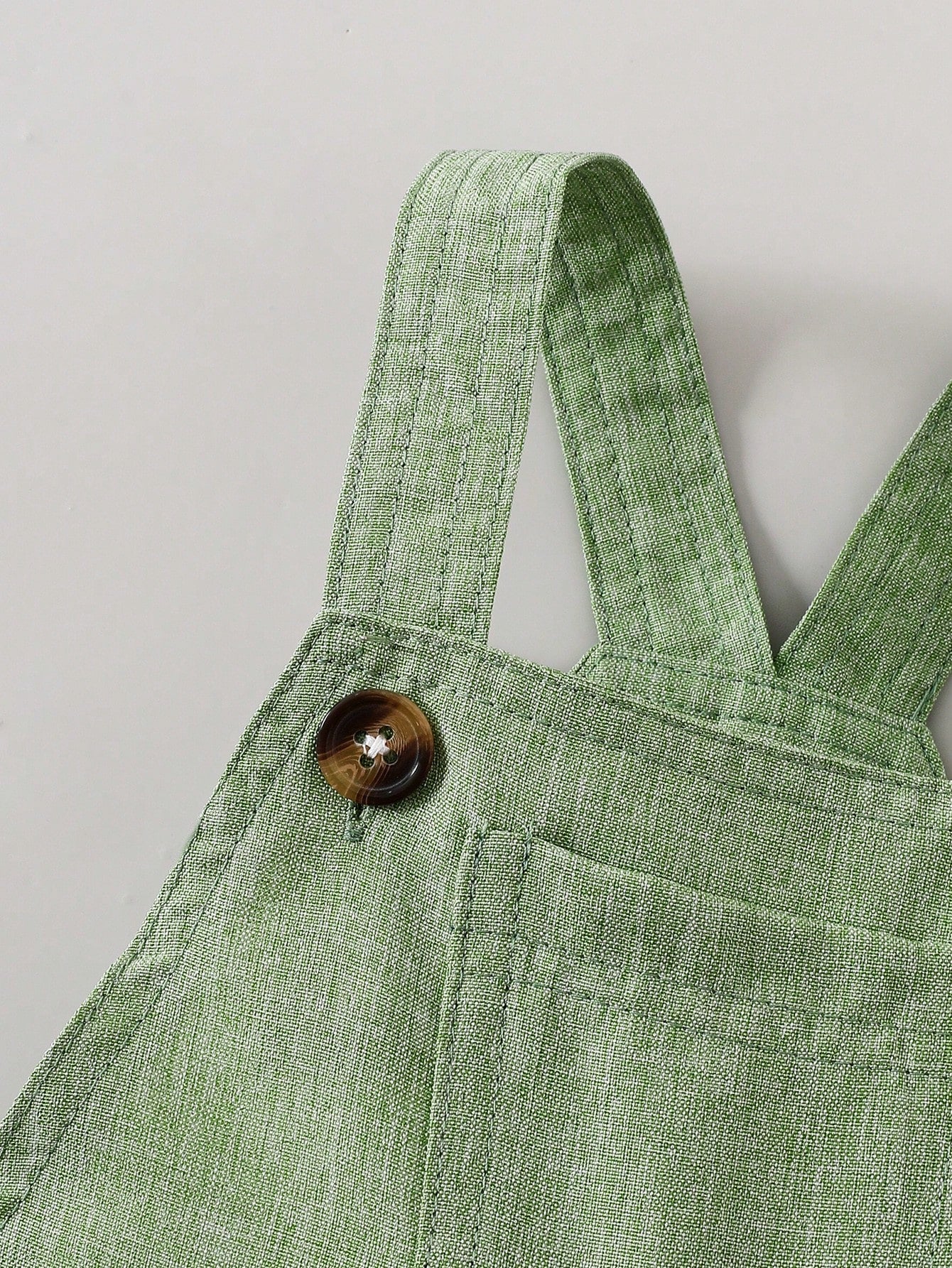 Prenda verde overol para bebe detalle de botones y tirantes