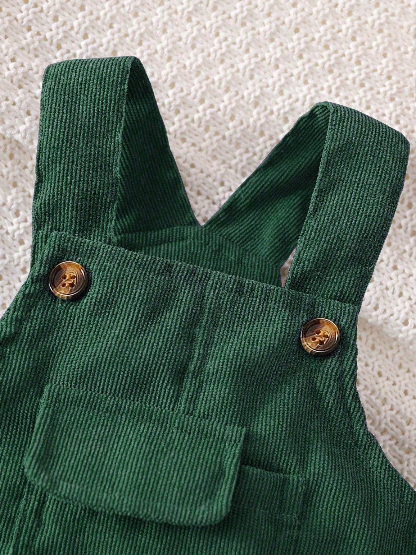 Prenda verde oscuro overol para bebe detalle del bolsillo frontal con solapa