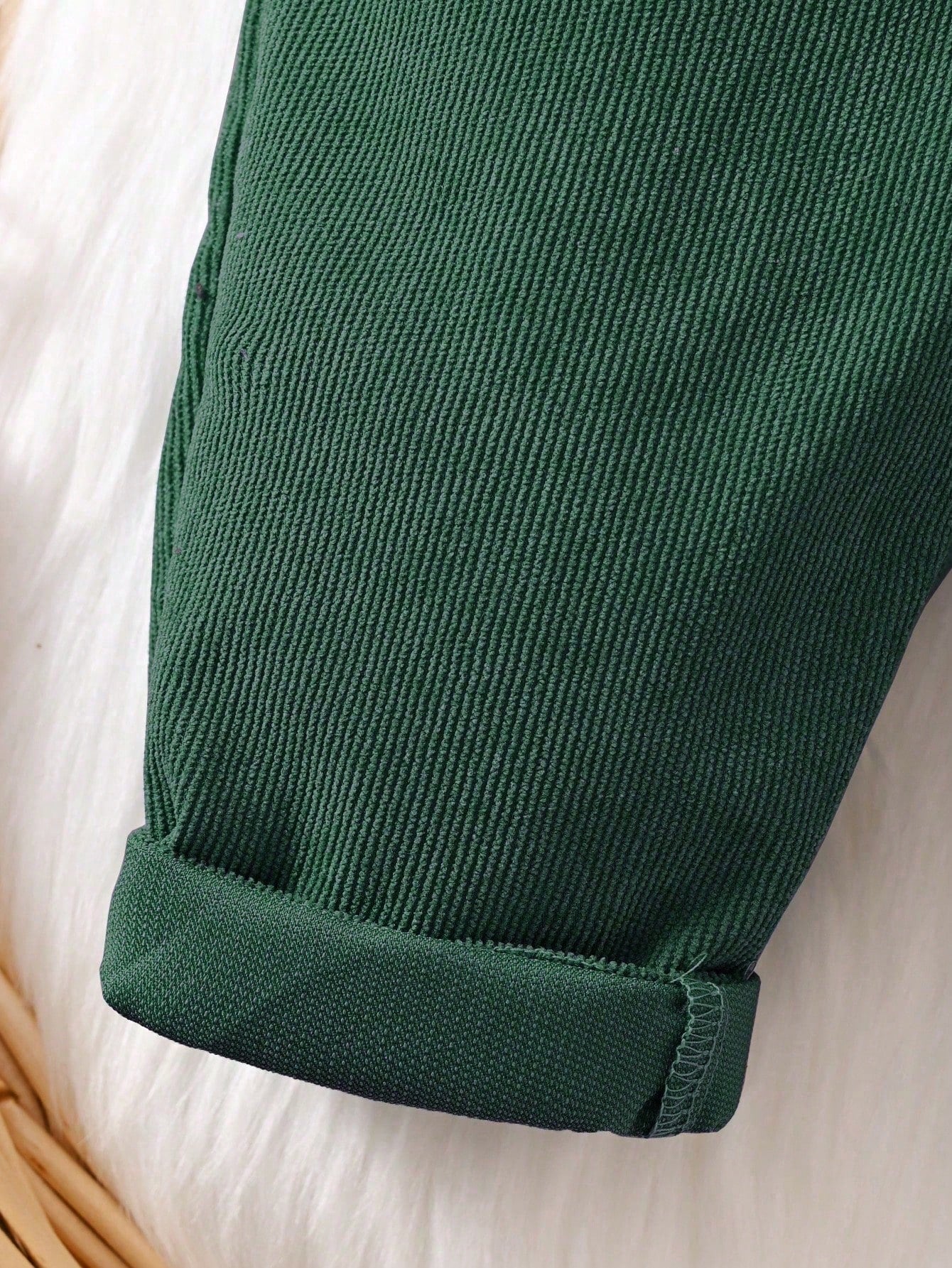 Prenda verde oscuro overol para bebe detalle de la tela de pana y bajos doblados