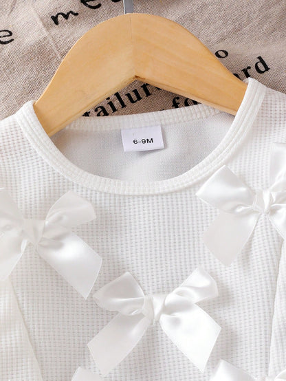 Prenda blanca conjunto para bebe con detalle de lazos 3D en la blusa