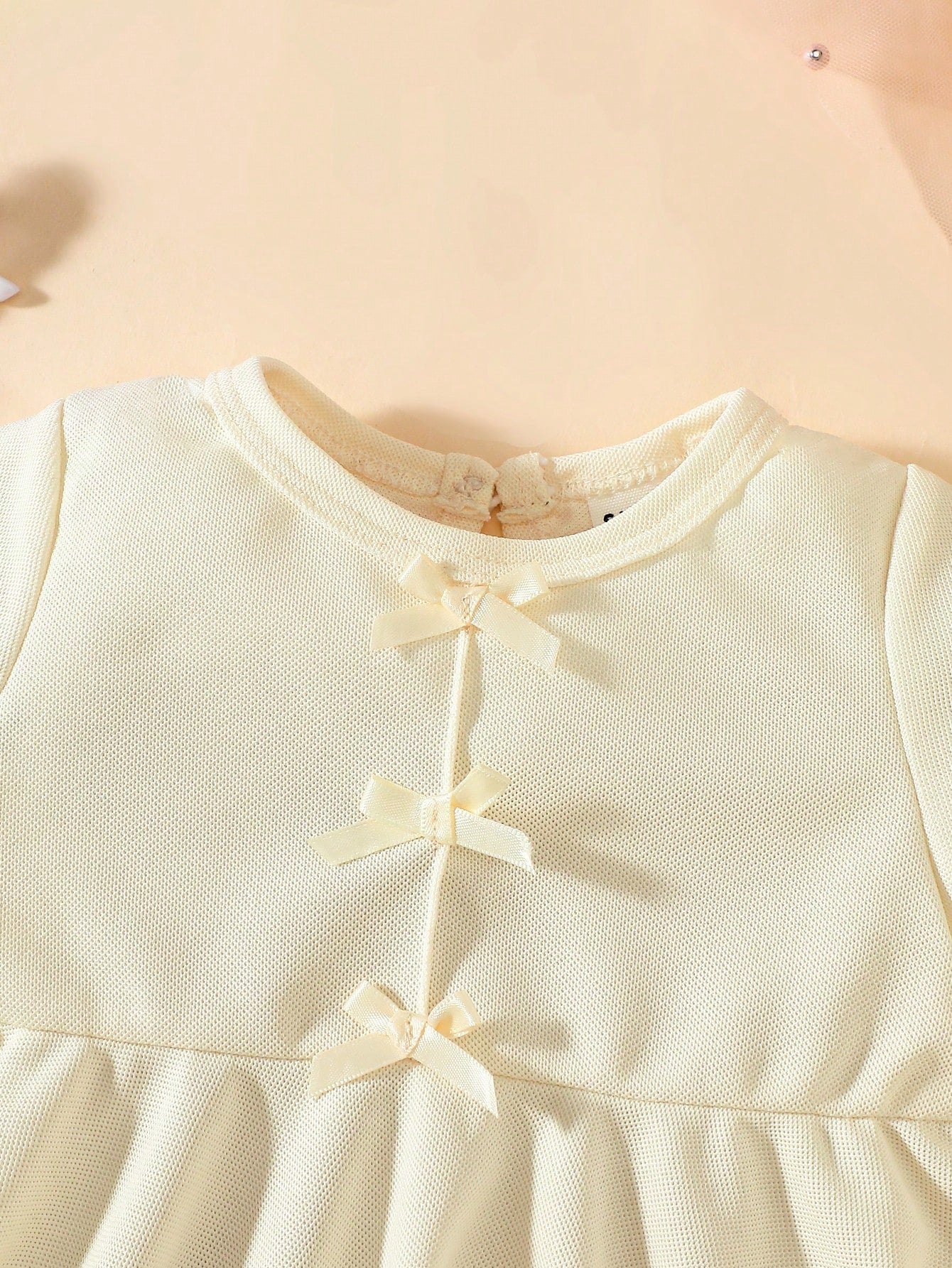 Prenda beige vestido para bebe detalle lazos frontales
