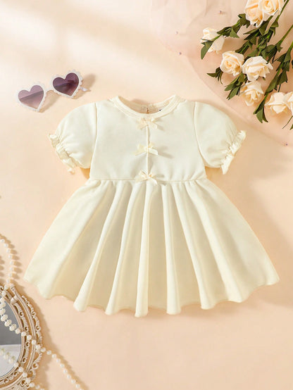 Prenda beige vestido para bebe con lazos decorativos vista frontal
