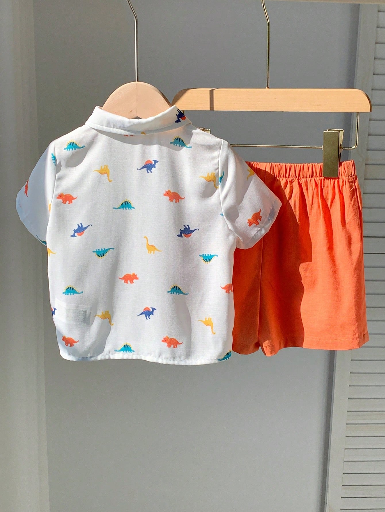 Prenda blanca conjunto para bebe con dinosaurios y short naranja vista trasera
