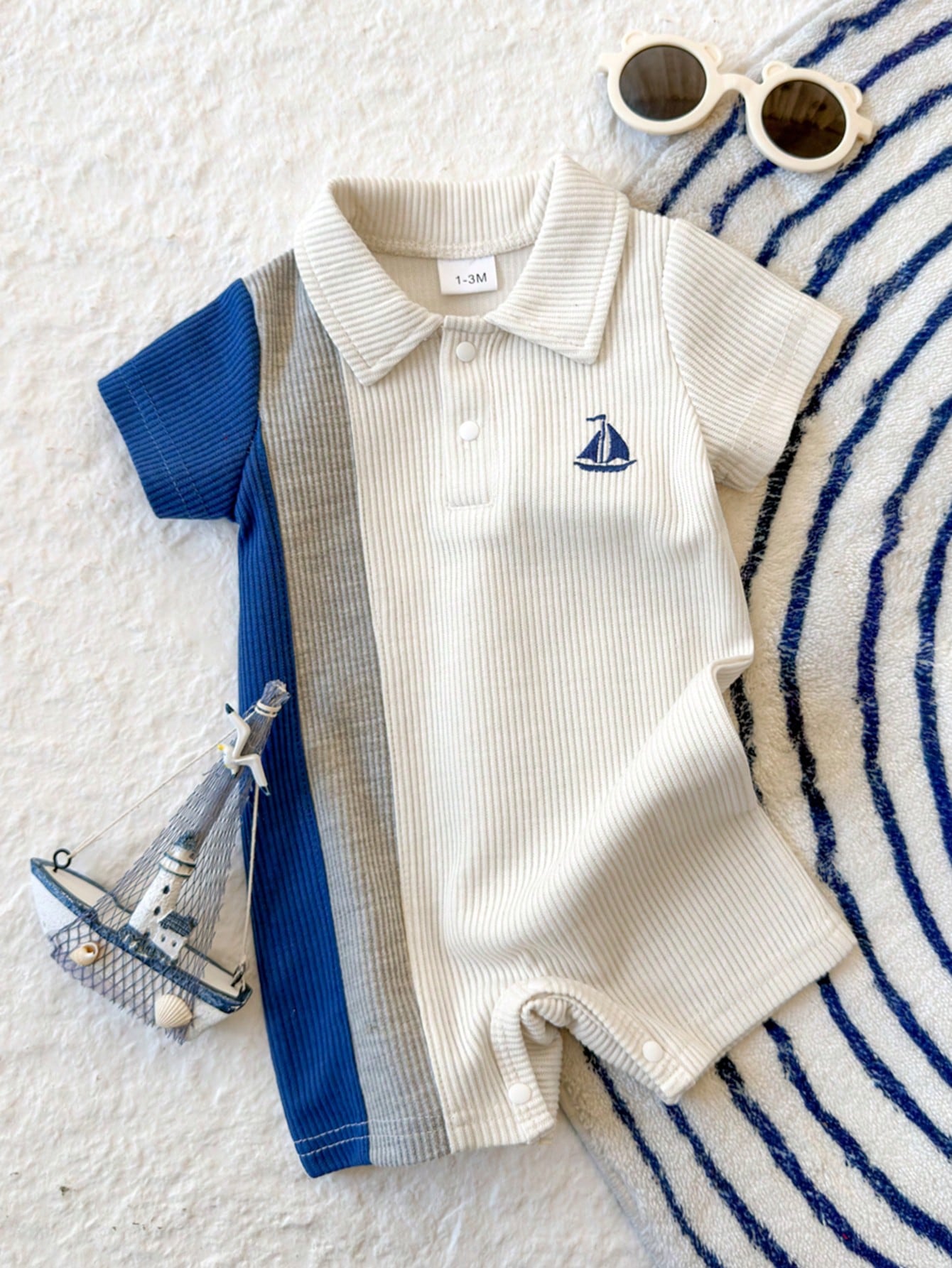 Prenda blanca pelele para bebe con bloques azul y gris y barco bordado vista frontal