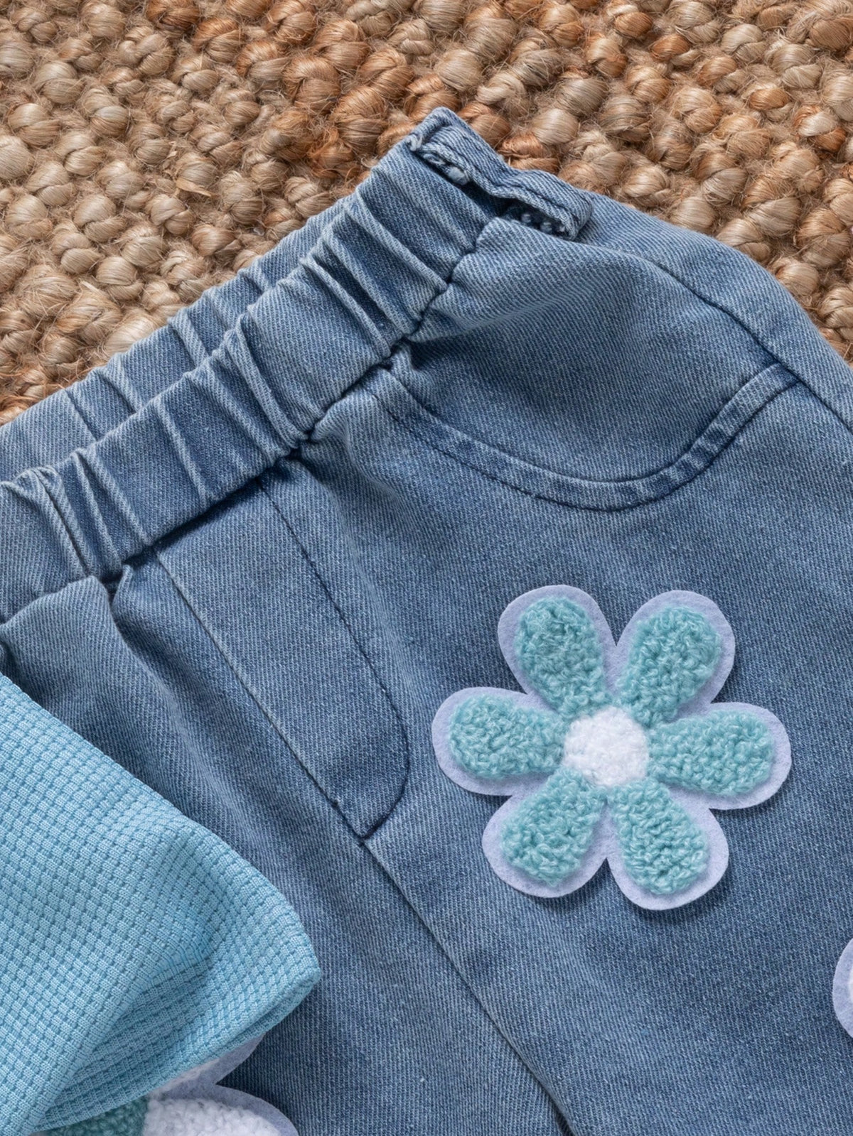 Pantalón azul de mezclilla para bebé con detalle de bolsillo, cintura elástica y flor celeste en relieve.