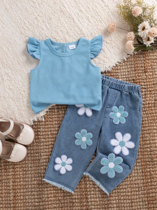 Conjunto celeste para bebé con blusa de volantes y pantalón de mezclilla con flores en relieve, vista frontal.