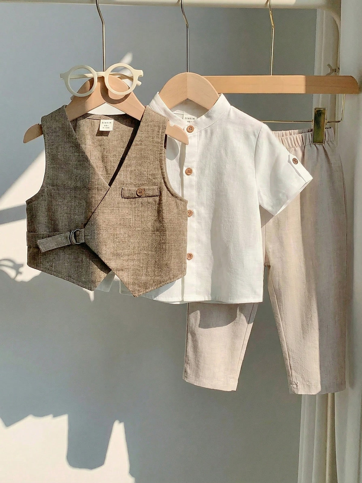 Conjunto beige para bebé con chaleco asimétrico, camisa blanca de manga corta y pantalón largo, vista frontal