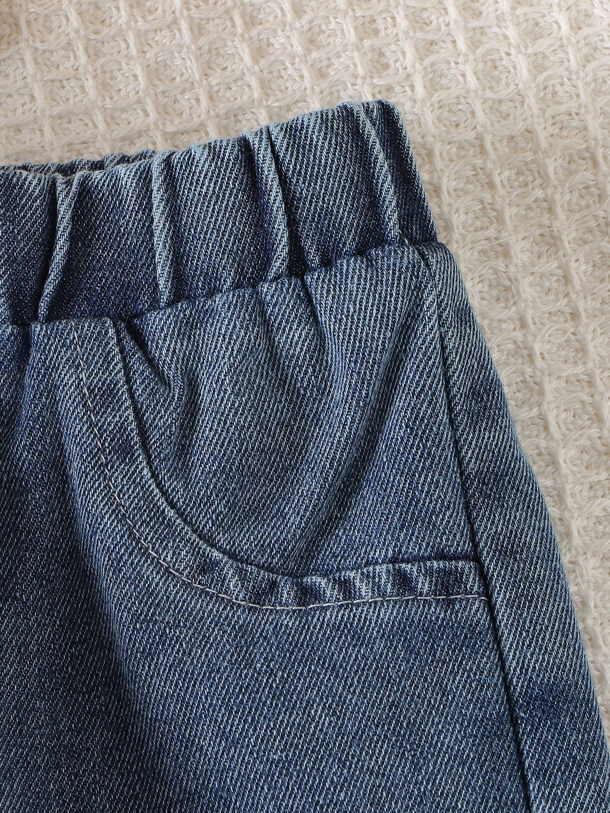 Pantalón de mezclilla azul para bebé con detalle de cintura elástica y bolsillo decorativo.