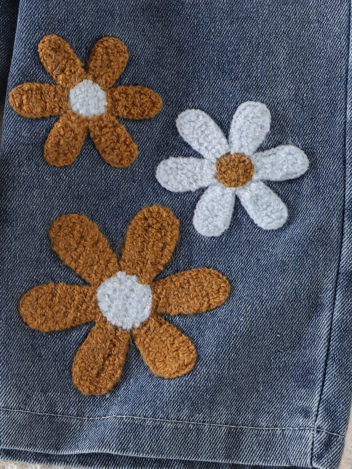 Pantalón azul de mezclilla para bebé con flores blancas y cafés en relieve, detalle de aplicaciones florales.