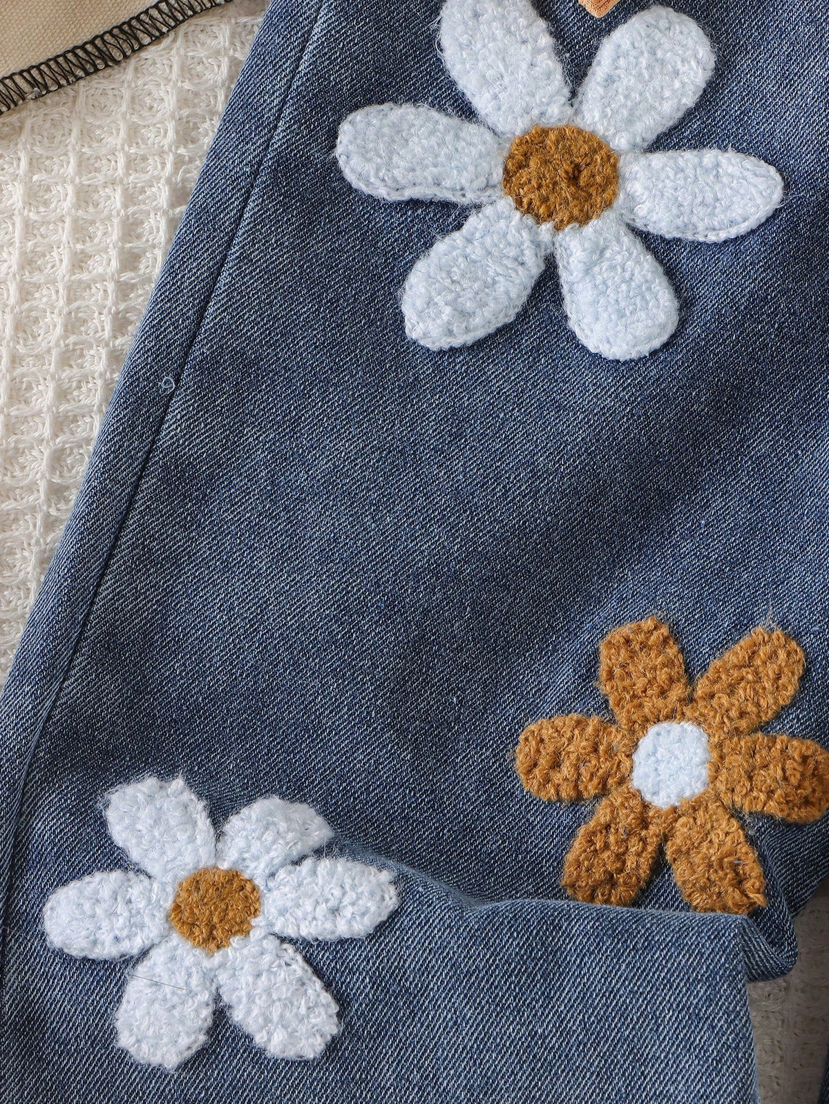 Pantalón azul para bebé con detalle de flores afelpadas en tonos blanco y café.