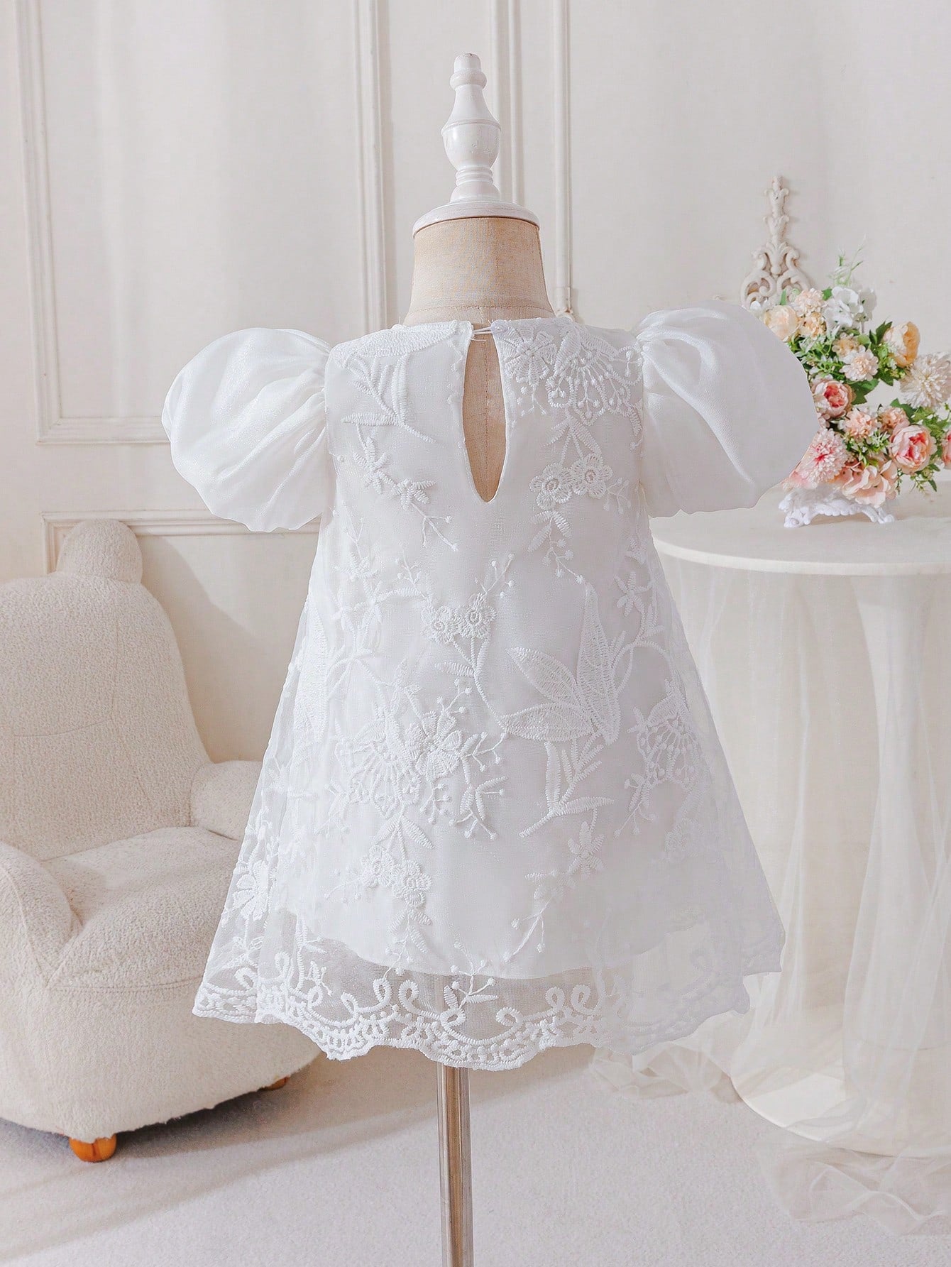 Prenda blanca vestido para bebe, vista posterior en maniquí con detalle de abertura trasera
