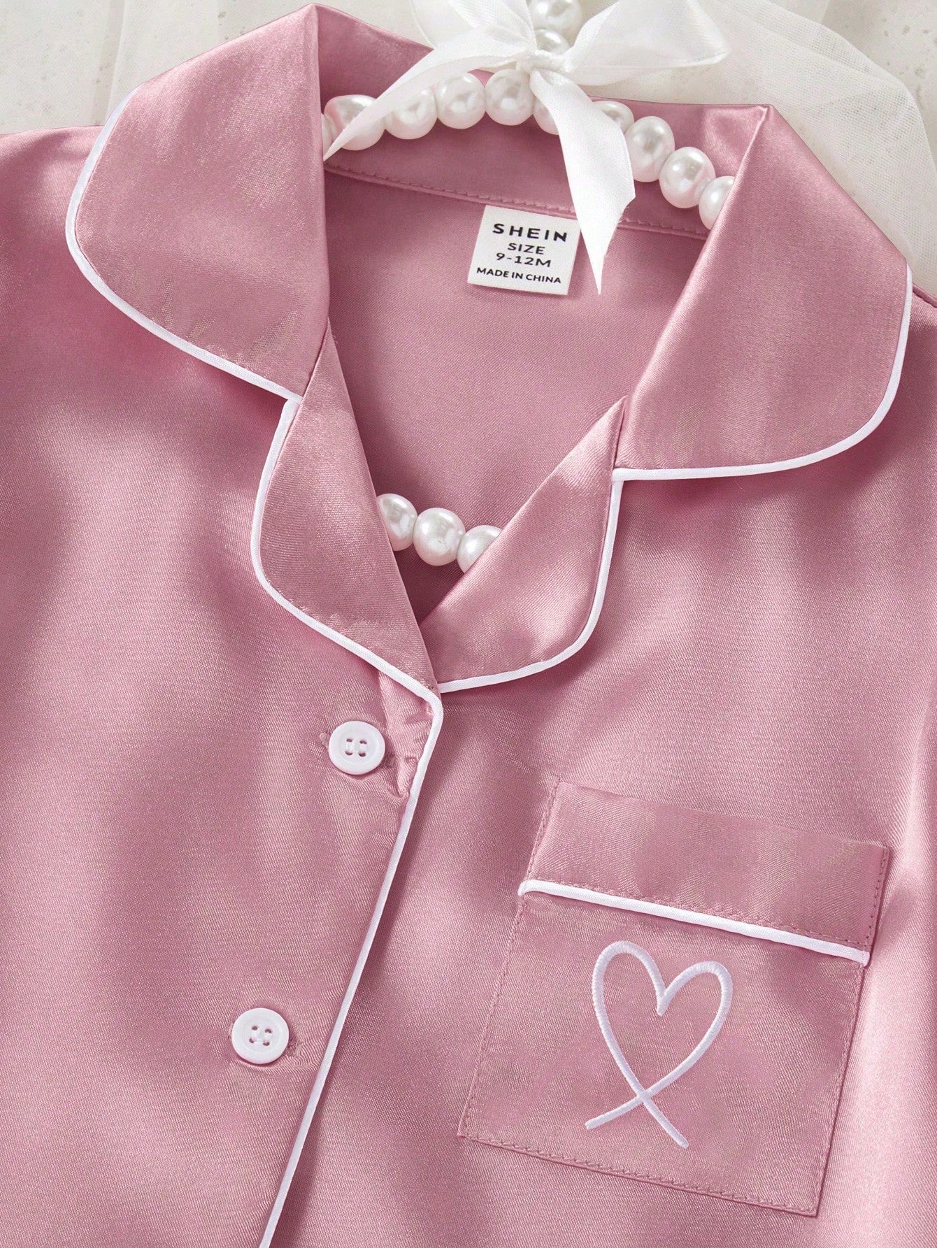 Prenda rosa pijama de satén para bebe con detalle de cuello, botones y bolsillo bordado