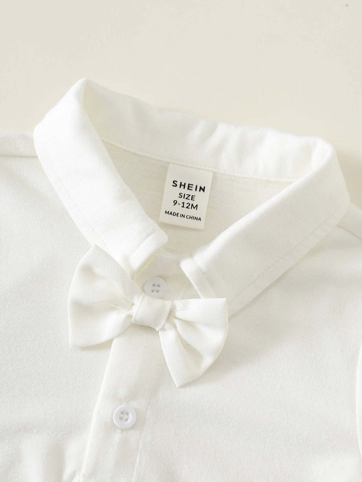 Camisa blanca para bebe con cuello camisero, pajarita decorativa y botones frontales, detalle del acabado.
