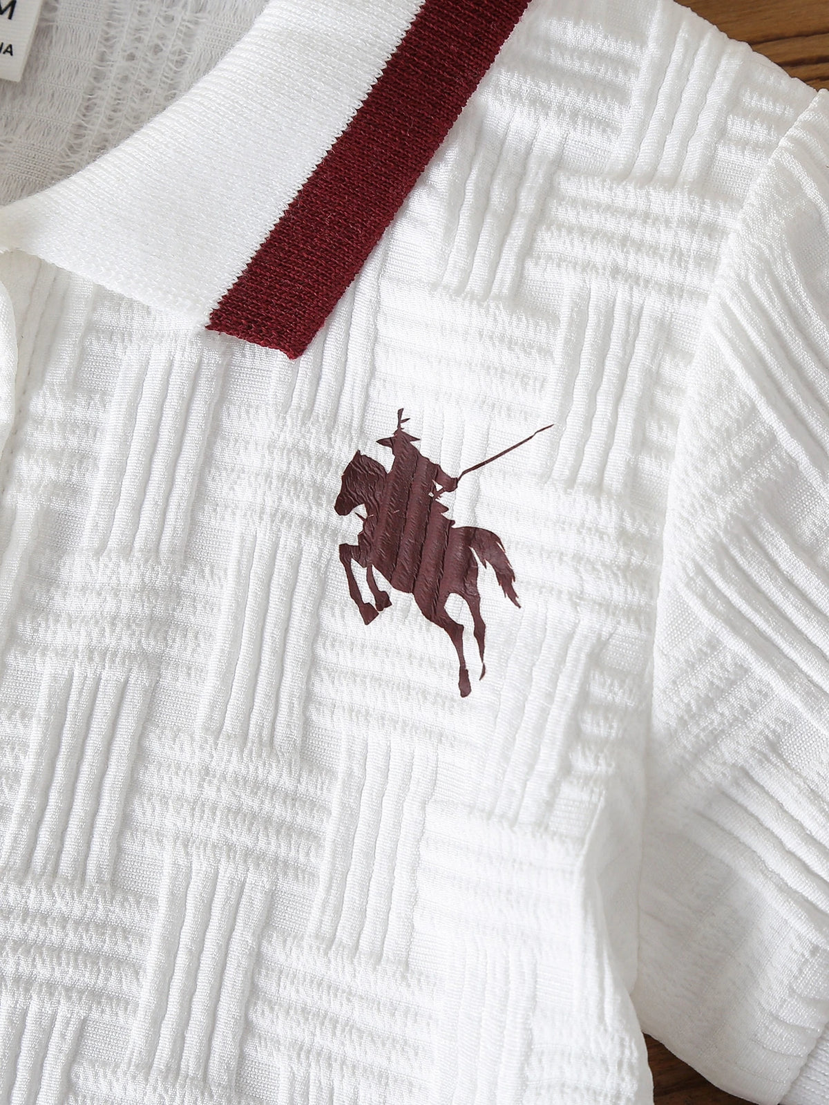 Camisa polo blanca para bebé con detalle de jinete a caballo y tejido texturizado.