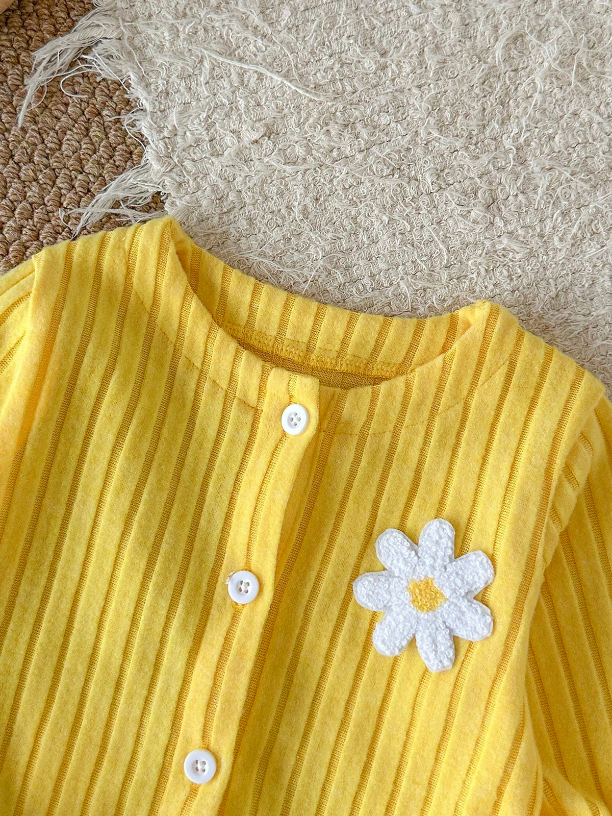 Chaqueta amarilla para bebe con botones blancos y flor en relieve, detalle del tejido acanalado
