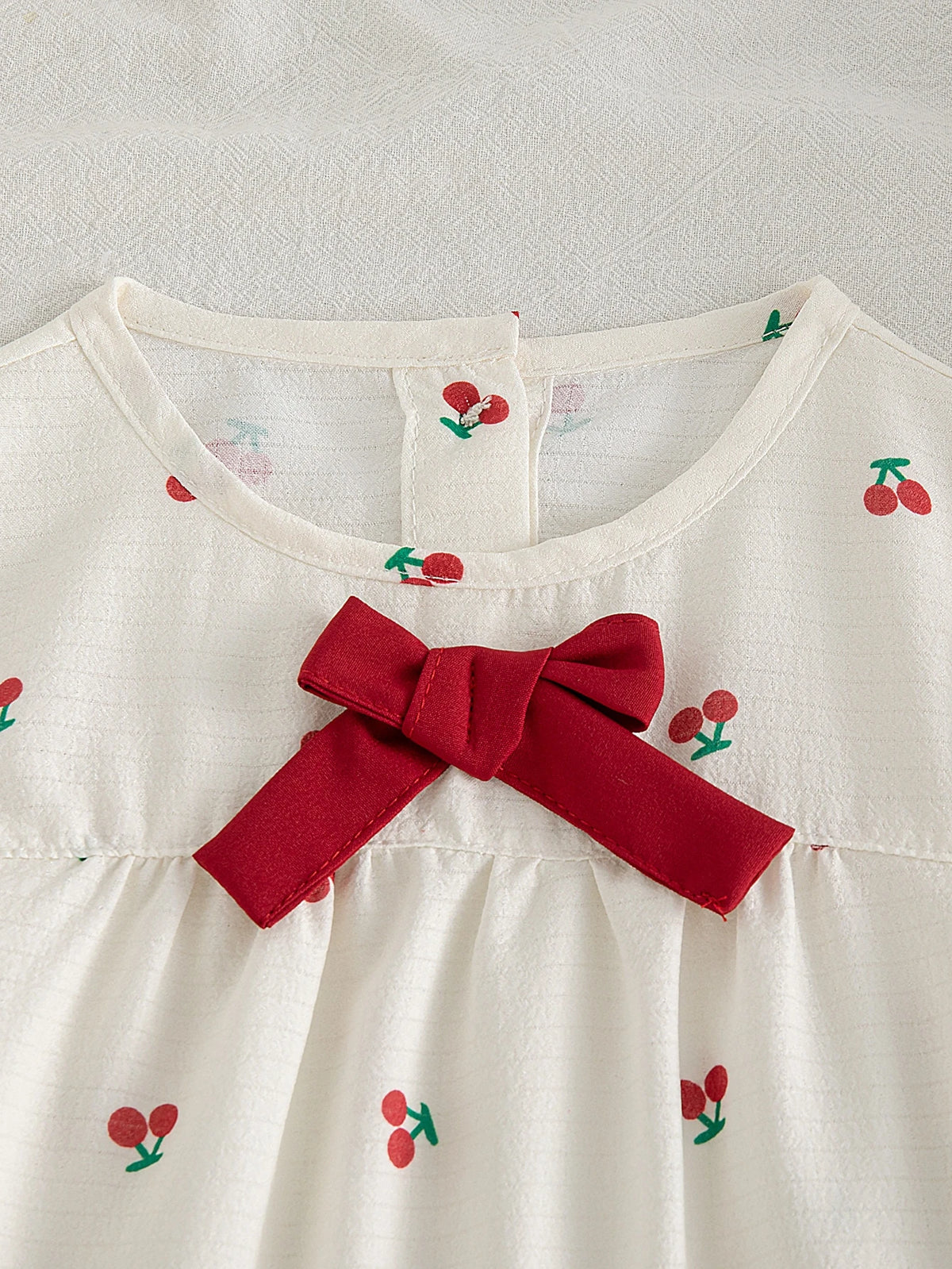 Blusa beige para bebe con estampado de cerezas y detalle de lazo rojo frontal