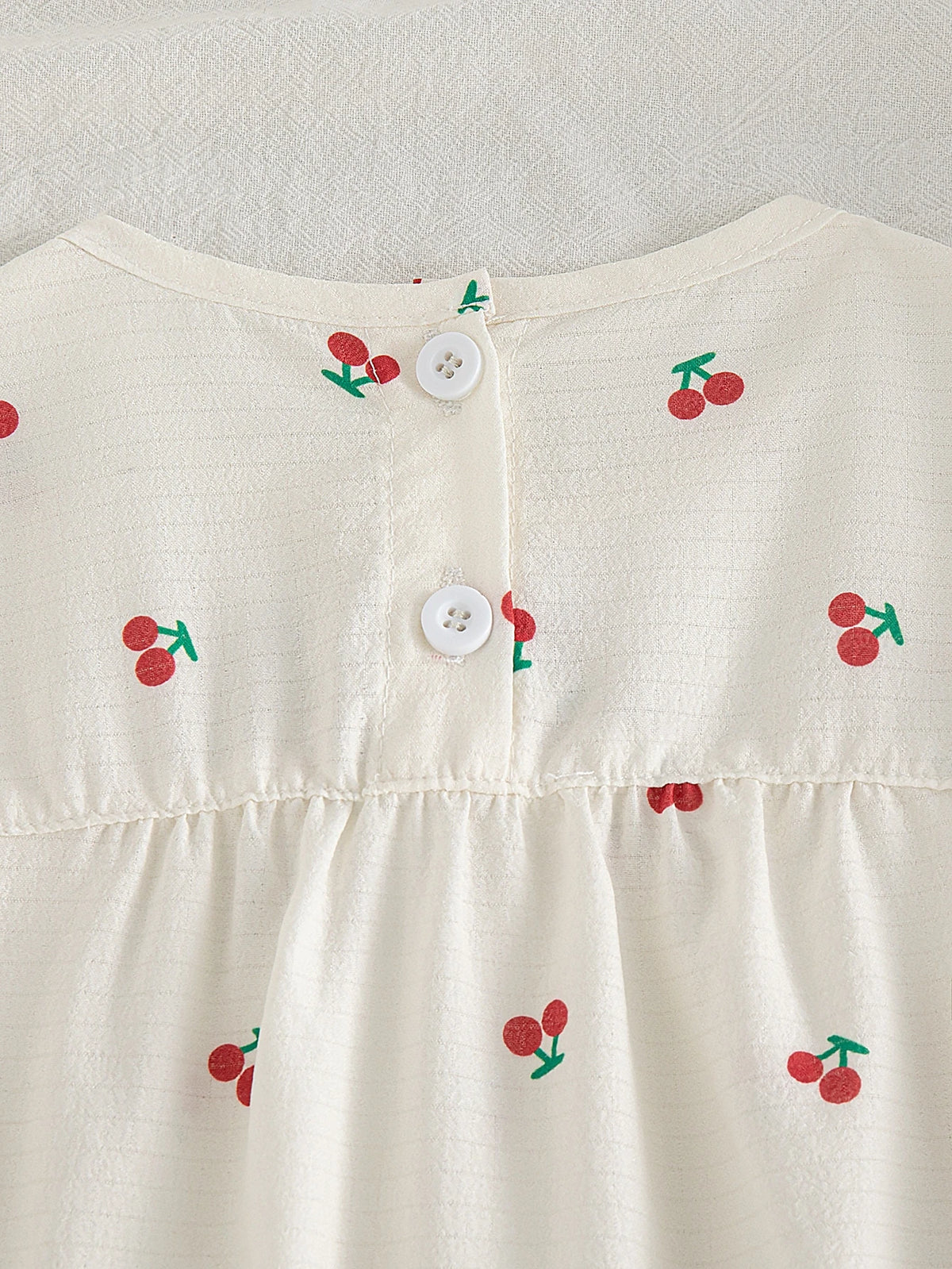 Blusa beige para bebe con cerezas y detalle de botones blancos posteriores