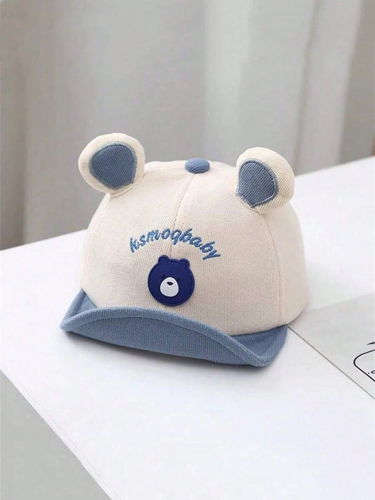 Gorro beige para bebe con orejitas azules y visera azul vista frontal
